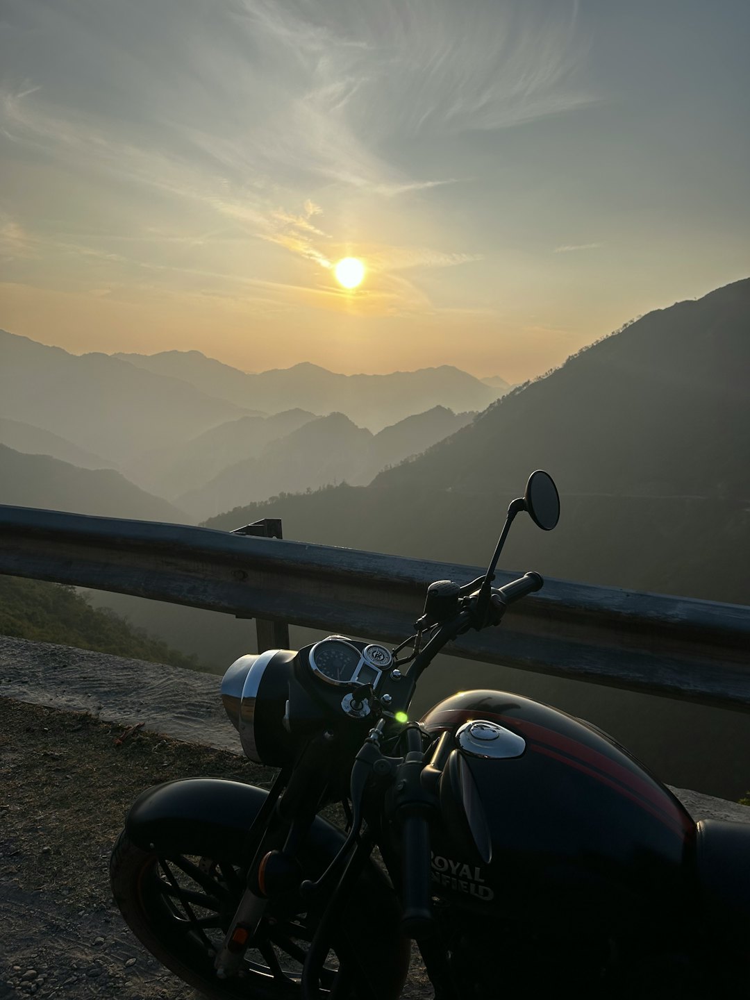 Motocicletta nera parcheggiata sul ciglio di una strada di montagna al tramonto.
